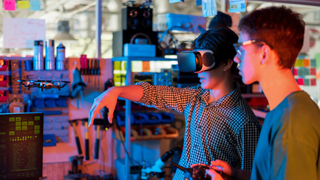 Laboratoire Fun Tech Adventures - Teens doing experiments in robotics in a laboratory. Boy in protective glasses and girl in VR headset controlling a flying drone using controller and hand. Red and blue illumination